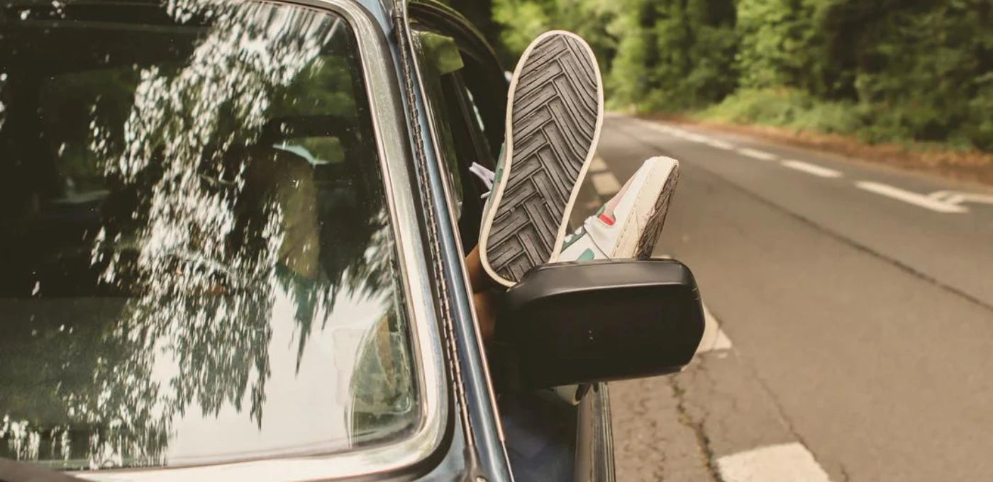Chaussures éco-responsable OTA à la fenêtre d'une voiture vintage sur une route goudronnée