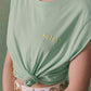 Tee-shirt en coton bio vert sans manche brodé soleil en jaune, porté par une femme et noué