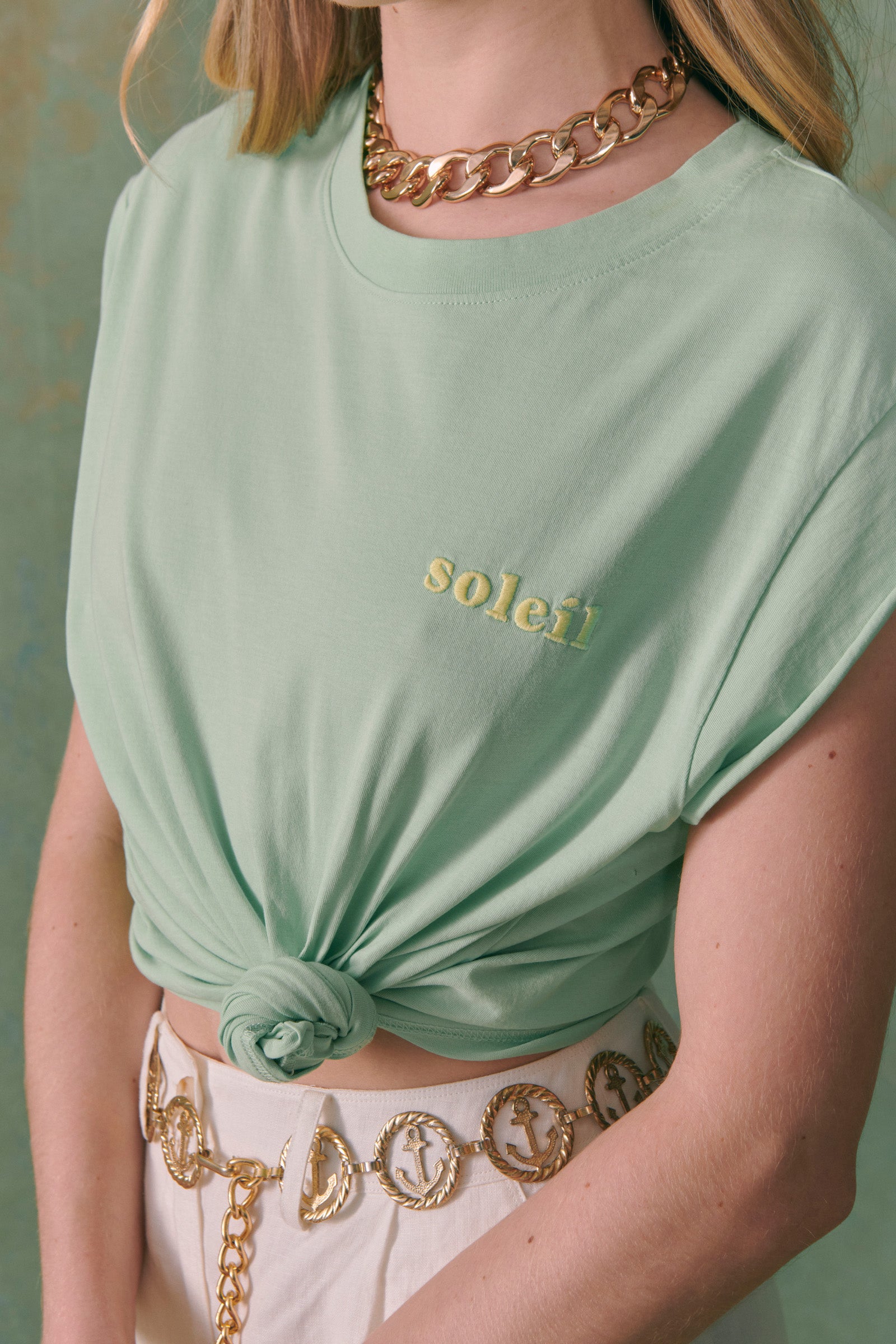Tee-shirt en coton bio vert sans manche brodé soleil en jaune, porté par une femme et noué