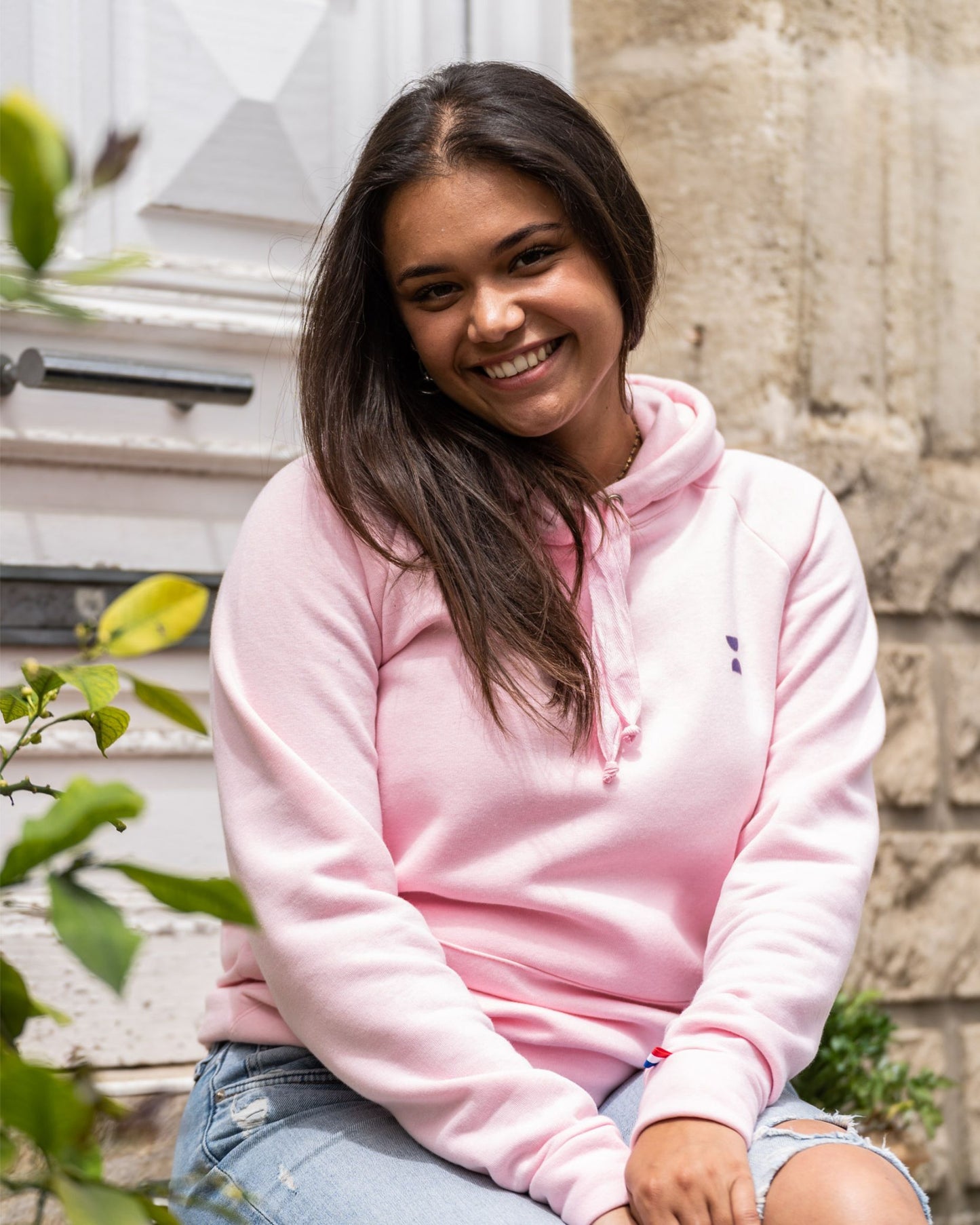 Femme assise en extérieur portant un hoodie rose éco-responsable fabriqué en France